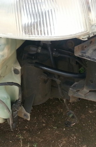 Už priekinio bamperio, dešnėje, šalia apiplovimo bakelio.